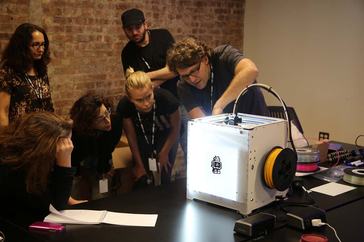 people gathered around a 3D printer while someone gives a demo